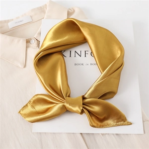 Detail of a ginger yellow satin scarf tied in a bow showing its soft glossy silk texture