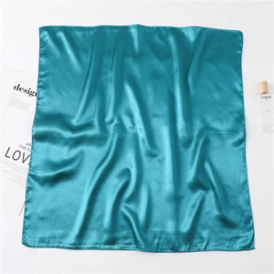 Peacock blue silk satin scarf shown folded next to a perfume bottle on white background