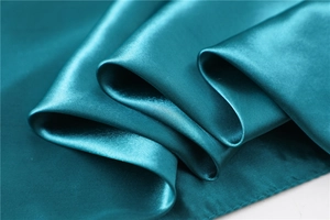 Close-up of smooth peacock blue silk satin fabric showing texture and soft sheen