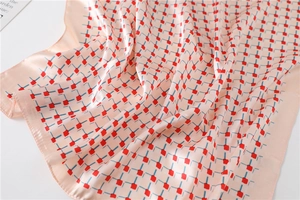 Detailed view of pink silk scarf with geometric red squares and blue stitch patterns