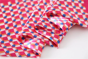 Macro shot of smooth satin scarf fabric showing pink geometric grid pattern and glossy texture