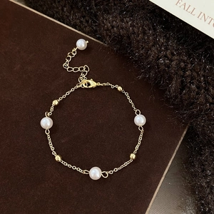 Detail of freshwater pearl bracelet with gold chain and lobster clasp on dark texture