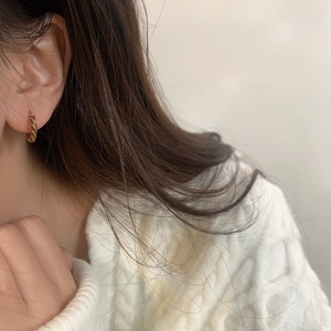 Détail d'une boucle d'oreille anneau torsadé doré avec un pull en maille crème chaleureux