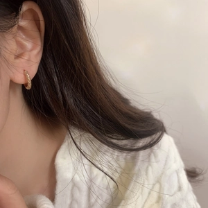 Gros plan d'une boucle d'oreille créole torsadée dorée portée par un mannequin en pull