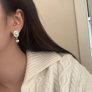 Détail d'une boucle d'oreille cœur vintage avec perle portée par un mannequin en pull blanc