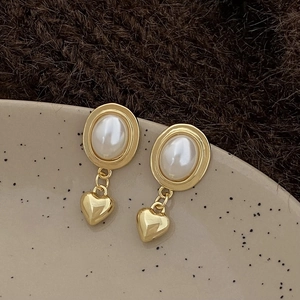 Détail de boucles d'oreilles cœur vintage dorées avec perles blanches sur un plat