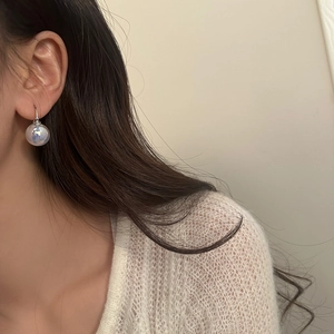 Macro shot of iridescent mermaid pearl earrings on model wearing white knit sweater