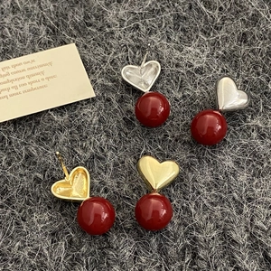 Elegant red heart pearl earrings with gold and silver metal accents on grey felt