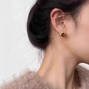 Boucles d'oreilles géométriques dorées avec perle marron portées avec une lumière chaude