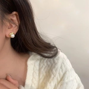 Gros plan d'une boucle d'oreille carrée dorée vintage avec perle blanche sur un mannequin