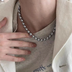 Detailed close-up of dark grey mirror pearl necklace worn with neutral layered outfit