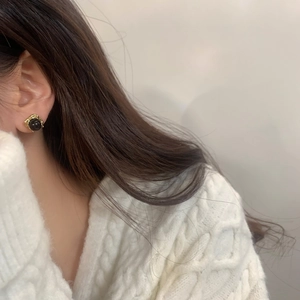 Gros plan de boucles d'oreilles rétro dorées avec perles noires portées sur un pull blanc