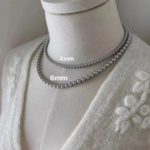 Comparison detail of 4mm and 6mm grey pearl necklaces on a model with knitwear