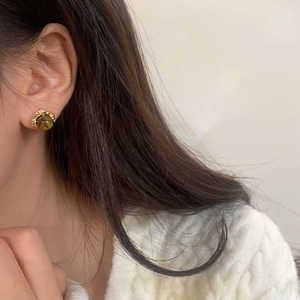 Gros plan de boucles d'oreilles vintage avec pierre œil de tigre portées avec un pull blanc