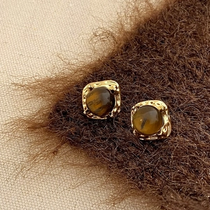 Gros plan de boucles d'oreilles dorées géométriques avec pierres brunes et martelées