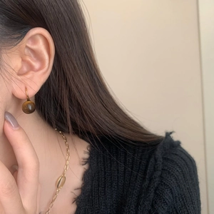 Close-up of vintage golden tiger eye stone drop earring on a female model wearing knitwear