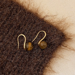 Macro detail of golden ear hooks with brown tiger eye stone beads on plush fabric