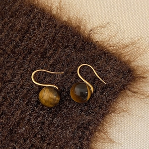 Detailed close-up of golden tiger eye stone drop earrings on warm brown velvet texture