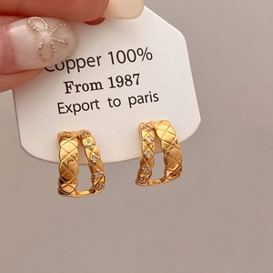 Macro view of gold U-shaped quilted copper earrings with sparkling zircon inlay detail