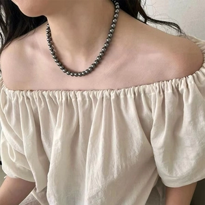 Elegant dark grey pearl necklace with round beads worn with an off-shoulder beige top