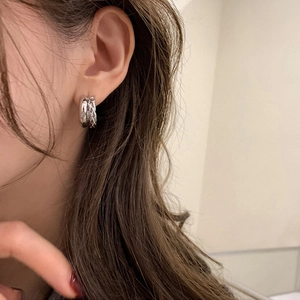 Détail de créoles argentées à triple couche torsadée portées sur le lobe de l'oreille