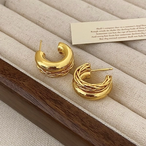 Détail de boucles d'oreilles créoles dorées avec design torsadé sur plateau velours
