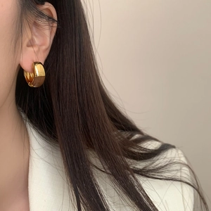 Gros plan d'une boucle d'oreille créole dorée en forme de C portée par un mannequin