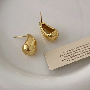 Macro-opname van gouden druppeloorbellen op keramisch blad met elegant minimalistisch metaal