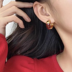 Gros plan d'une boucle d'oreille dorée en forme de C avec émail brun rouge sur un modèle