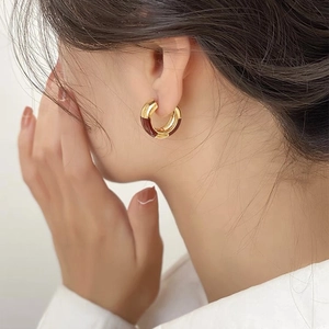 Gros plan d'une femme portant des boucles d'oreilles créoles dorées et émail brun rouge