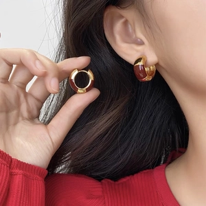 Close-up of elegant burgundy enamel hoop earrings in gold setting worn by model