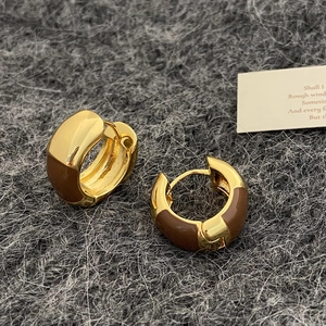 Détail macro de boucles d'oreilles créoles dorées et émail marron sur tricot