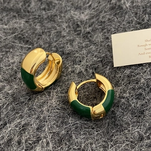 Détail de boucles d'oreilles créoles C dorées avec émail vert foncé sur tissu gris