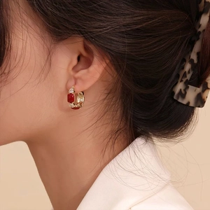 Close-up of elegant gold hoop earrings with red and clear square zircons on model ear