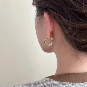 Detailed side view of a gold-plated hoop earring with textured ripples on female model