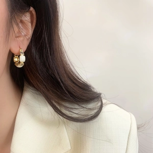 Elegant gold earrings with white enamel and sparkling zircons worn by a model