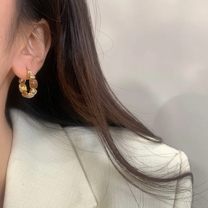 Close-up of elegant gold hoop earrings with brown zircons worn on a model in tweed jacket
