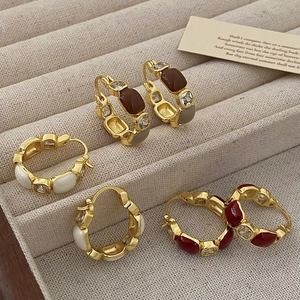 Macro detail of vintage enamel and zircon hoop earrings in gold setting on linen tray