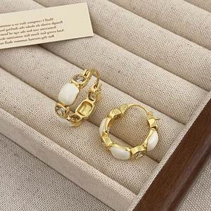 Detail of gold-plated earrings with white enamel and clear zircon studs in a jewelry tray