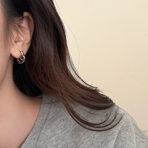 Close-up of a twisted heart-shaped silver earring showing polished metallic texture on ear