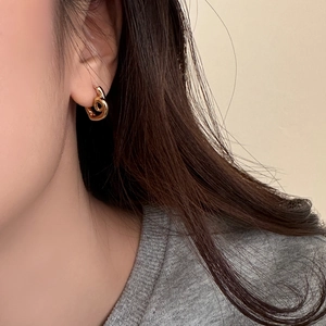 Detail of model wearing golden twisted hoop earrings with a minimalist knot design