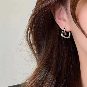 Close-up of silver metal heart earrings worn by a model showing a dual-layer design