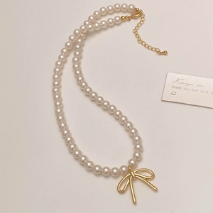Detail of elegant pearl necklace featuring a golden bow pendant and adjustable clasp