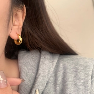 Detail of chunky teardrop gold hoop earrings with polished finish on model