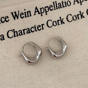 Close-up of geometric silver U-shaped earrings on textured fabric background