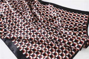 Macro view of geometric plaid silk scarf with satin finish and black border detail