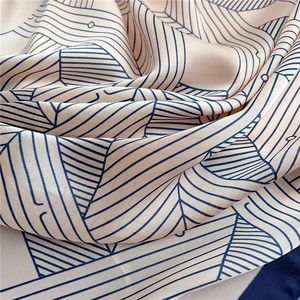 Detail of silk scarf with geometric blue lines on beige fabric showing soft texture