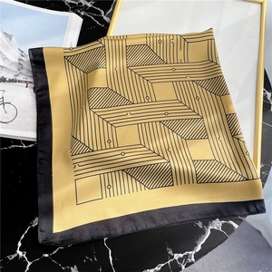 Close-up of a golden silk scarf with black geometric lines on marble background
