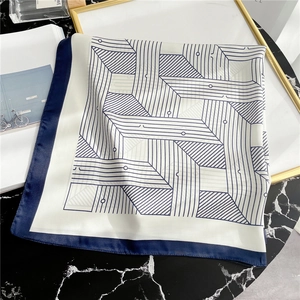 Close-up of geometric striped silk scarf with navy blue borders on marble surface