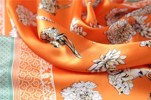 Close-up of orange silk scarf showing elegant floral print and smooth satin texture
